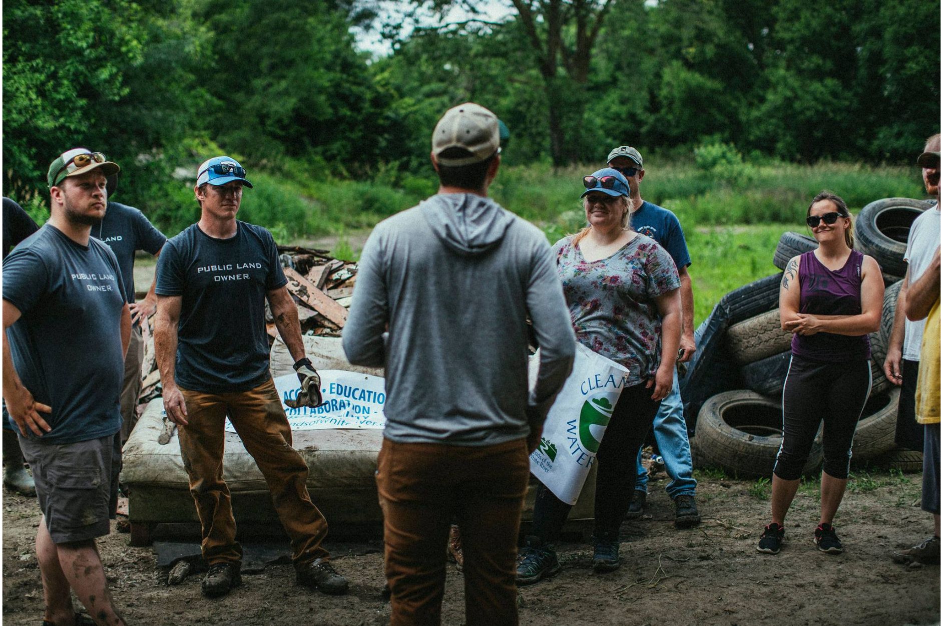 A group of volunteers wearing gloves stand outside listening to a speaker.