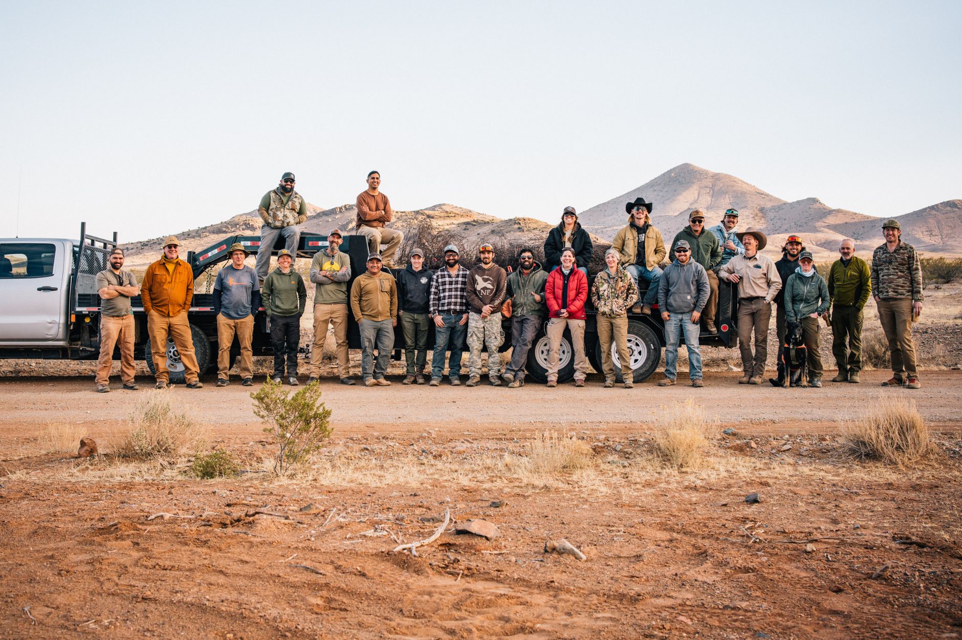 A group of volunteers stand against a truck and trailer in the desert.